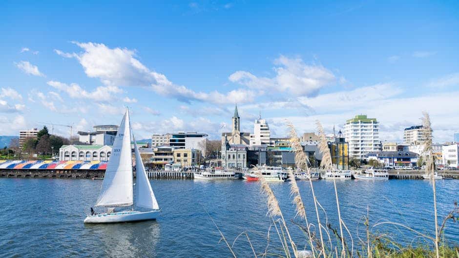 Beautiful day at the Valdivia waterfront in Chile, featuring a sailboat and urban skyline.