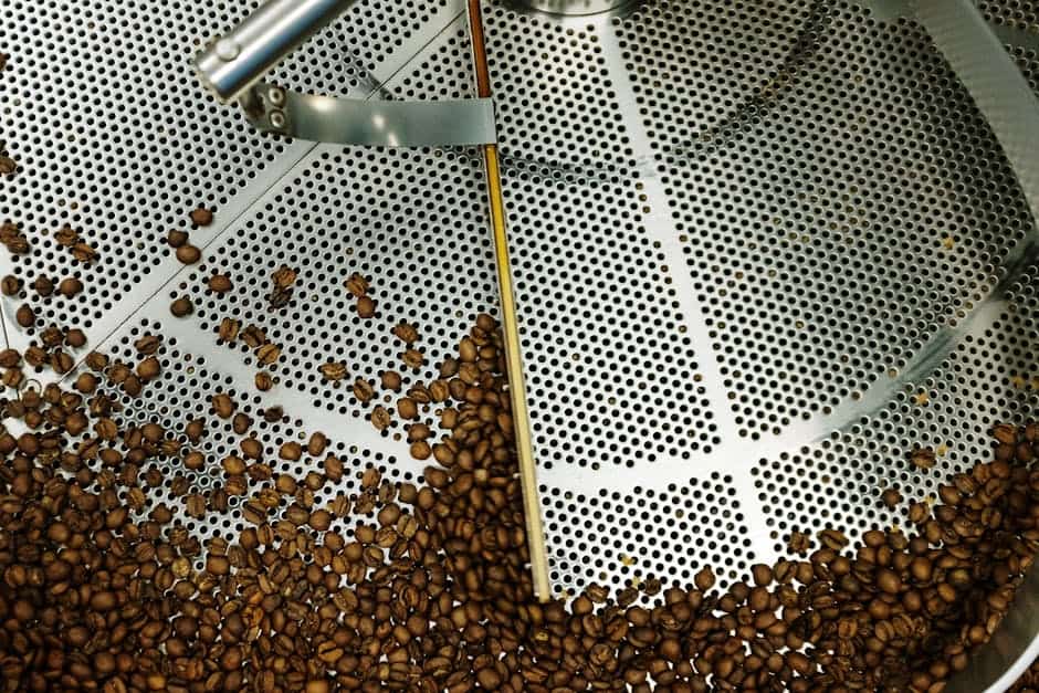 Top view of coffee beans roasting in an industrial steel machine.