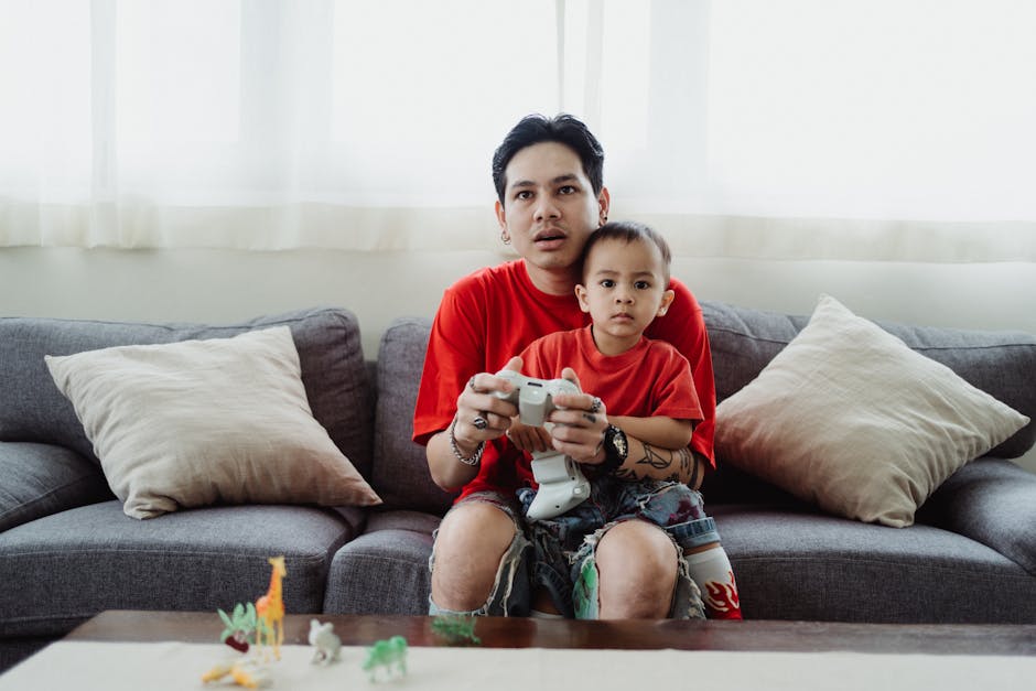 Father and son playing video games on a couch wearing matching outfits, showcasing family bonding.