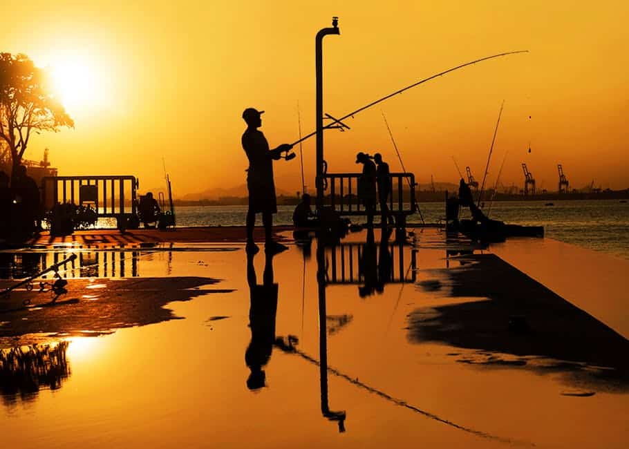 Fishermen cast silhouettes against a glowing orange sunset in Rio de Janeiro, creating a serene and reflective scene.