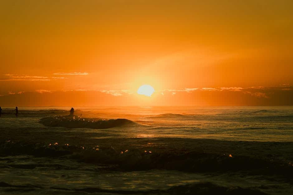 A tranquil sunset over the ocean with silhouetted surfers riding gentle waves.