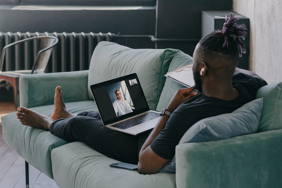 African American man relaxes on a couch while video chatting on a laptop, enjoying a casual day indoors.