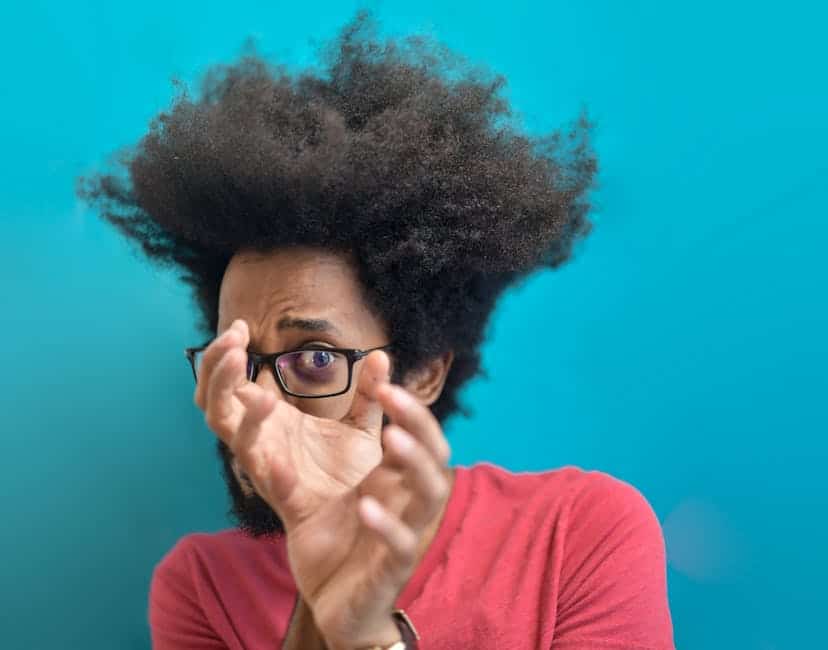 Astonished man with afro hairstyle and glasses in front of a blue background.