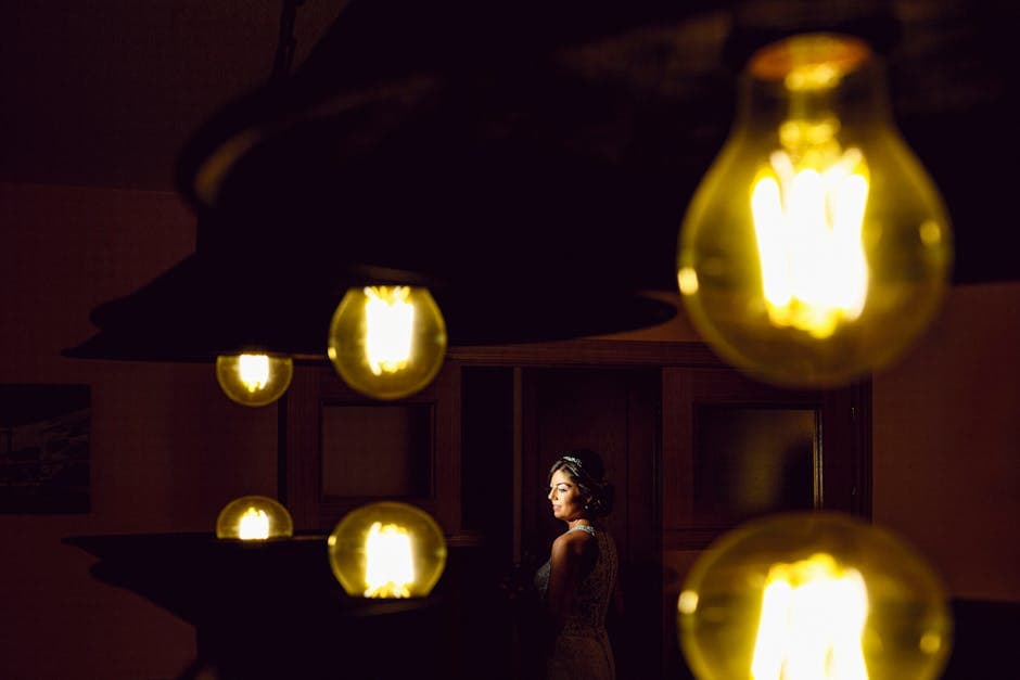 A bride poses elegantly in dramatic lighting surrounded by glowing bulbs, creating a unique wedding portrait.