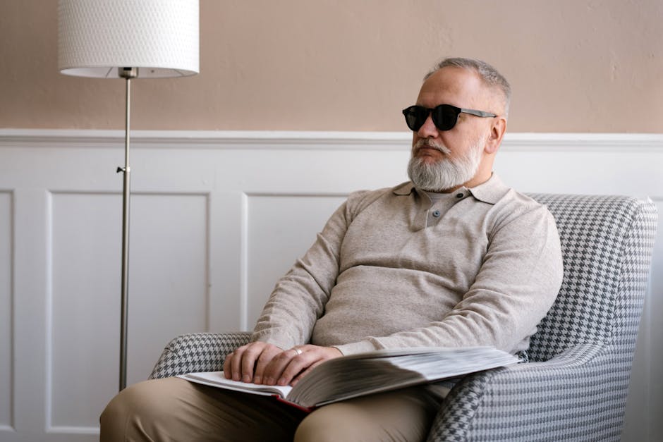 Senior man with sunglasses reading a braille book in a cozy modern interior.
