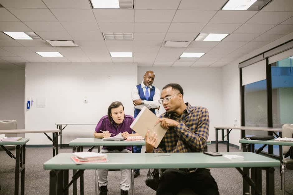 Students in a classroom secretly talking while a teacher observes from behind.