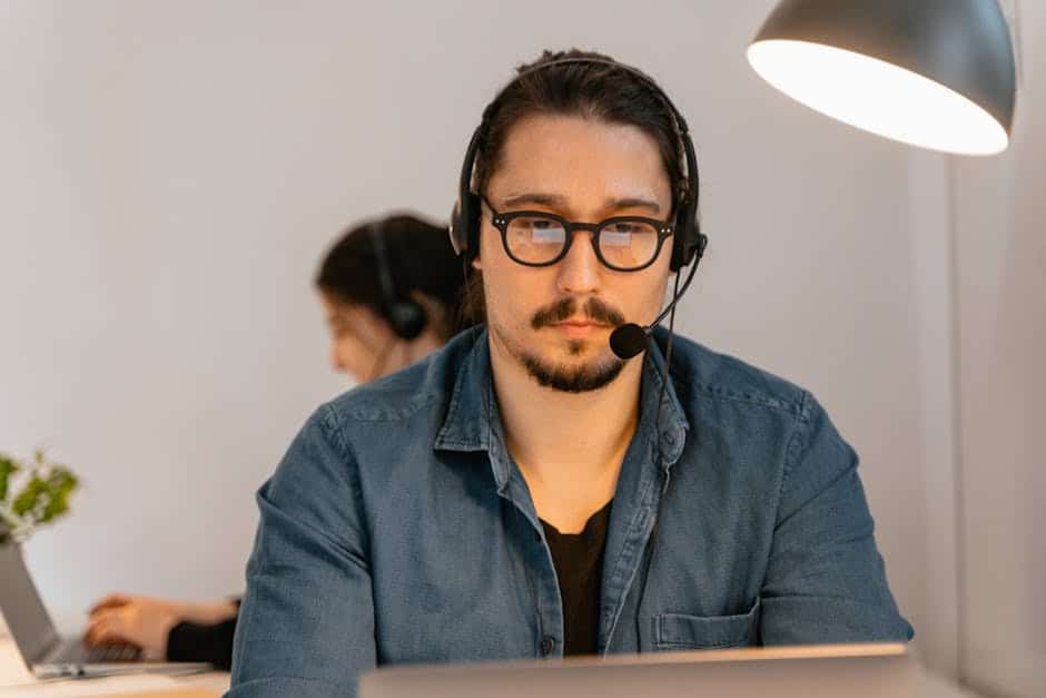 A call center agent wearing headphones, working intently at his desk in a modern office environment.
